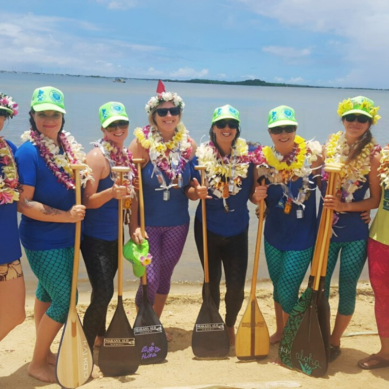 Photo of 8 women holding kayak paddles standing on a beach